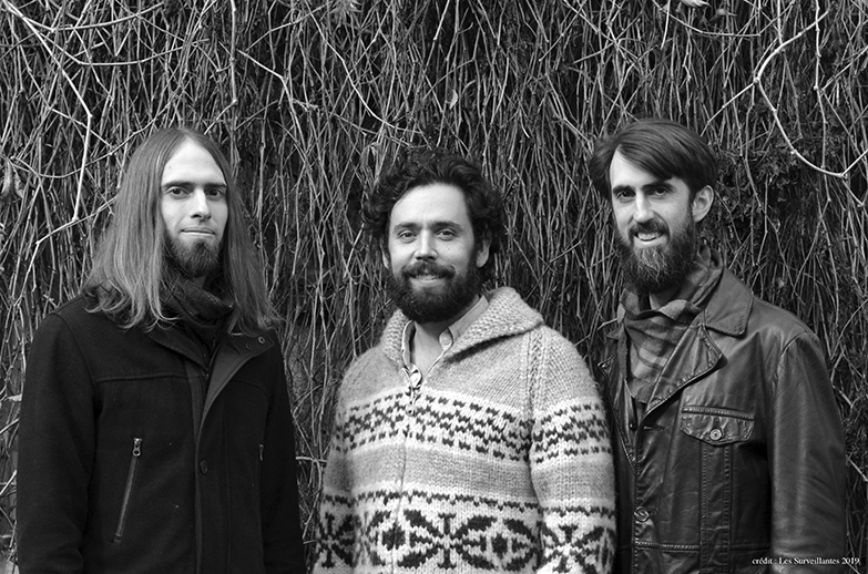 Three members of Les Surveillantes standing in front of a tree 